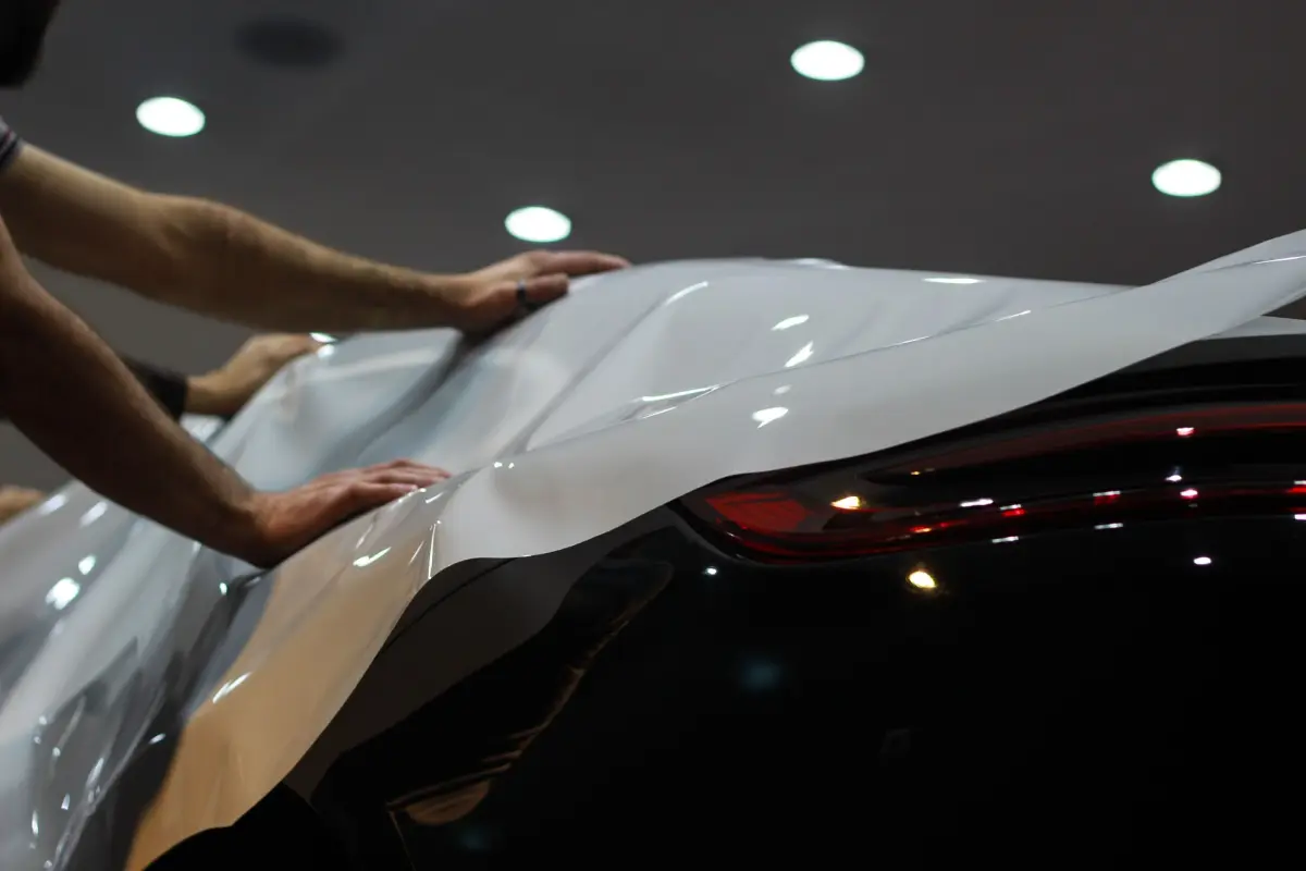 Installers laying a full sheet of paint protection film over a black car